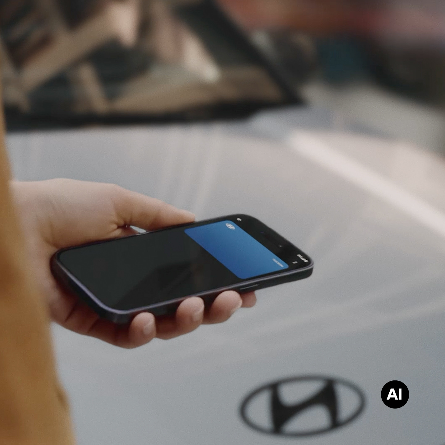 A close-up view of a hand holding a mobile phone with the background of the Hyundai BAYON N Line.