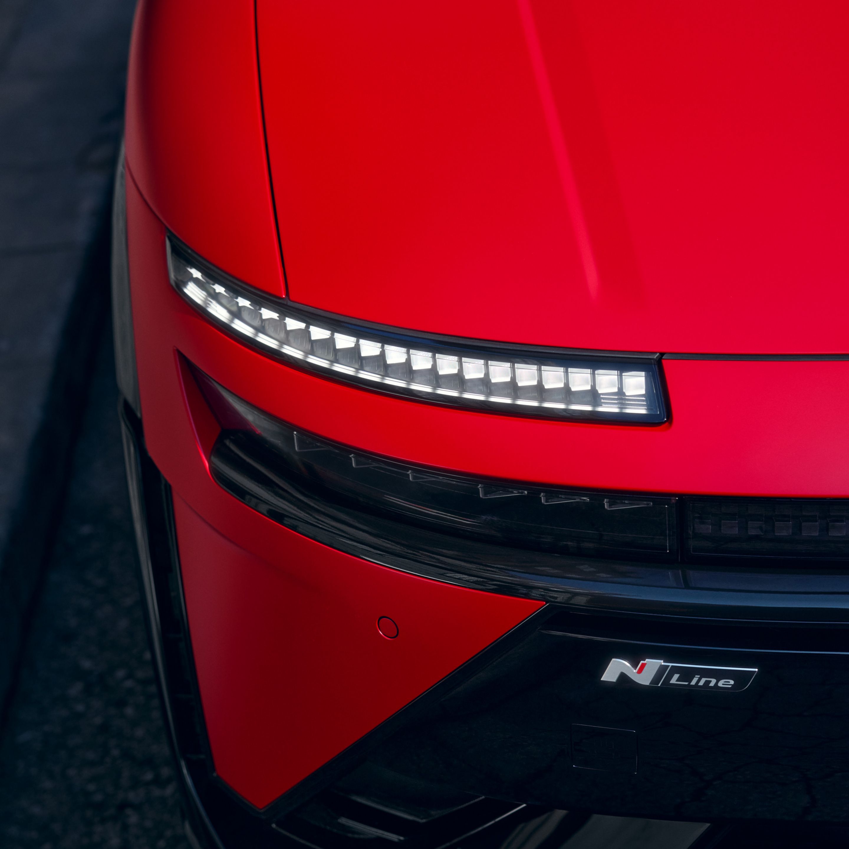 Red Hyundai IONIQ 3 front detail showing slim LED light strip and N Line badge on sculpted body.
