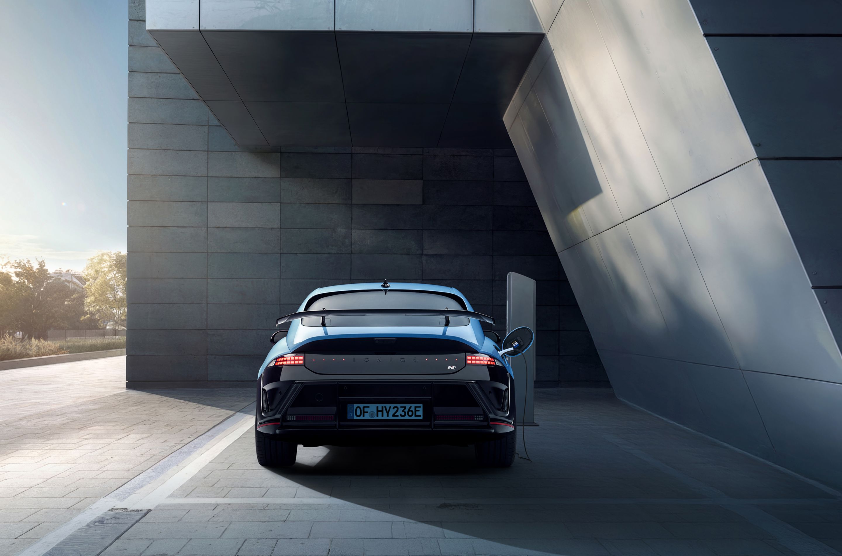 Hyundai IONIQ 6 N modern épület mellett parkol, nyitott vezető oldali ajtóval. Hátulnézetből.