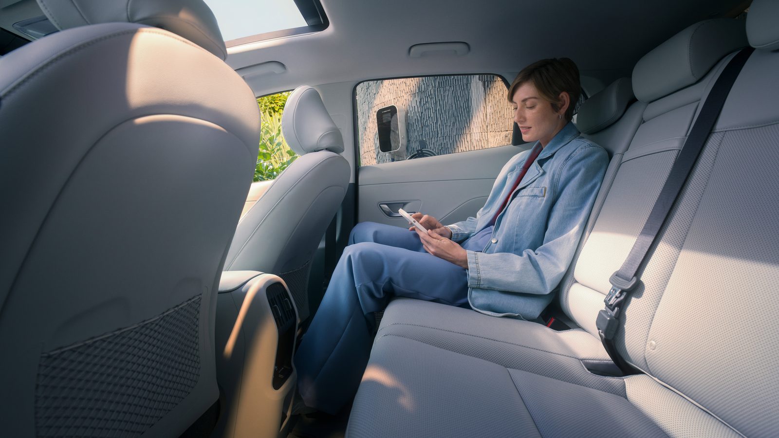 Egy hölgy a Hyundai KONA hátsó ülésén okostelefonjára pillant.
