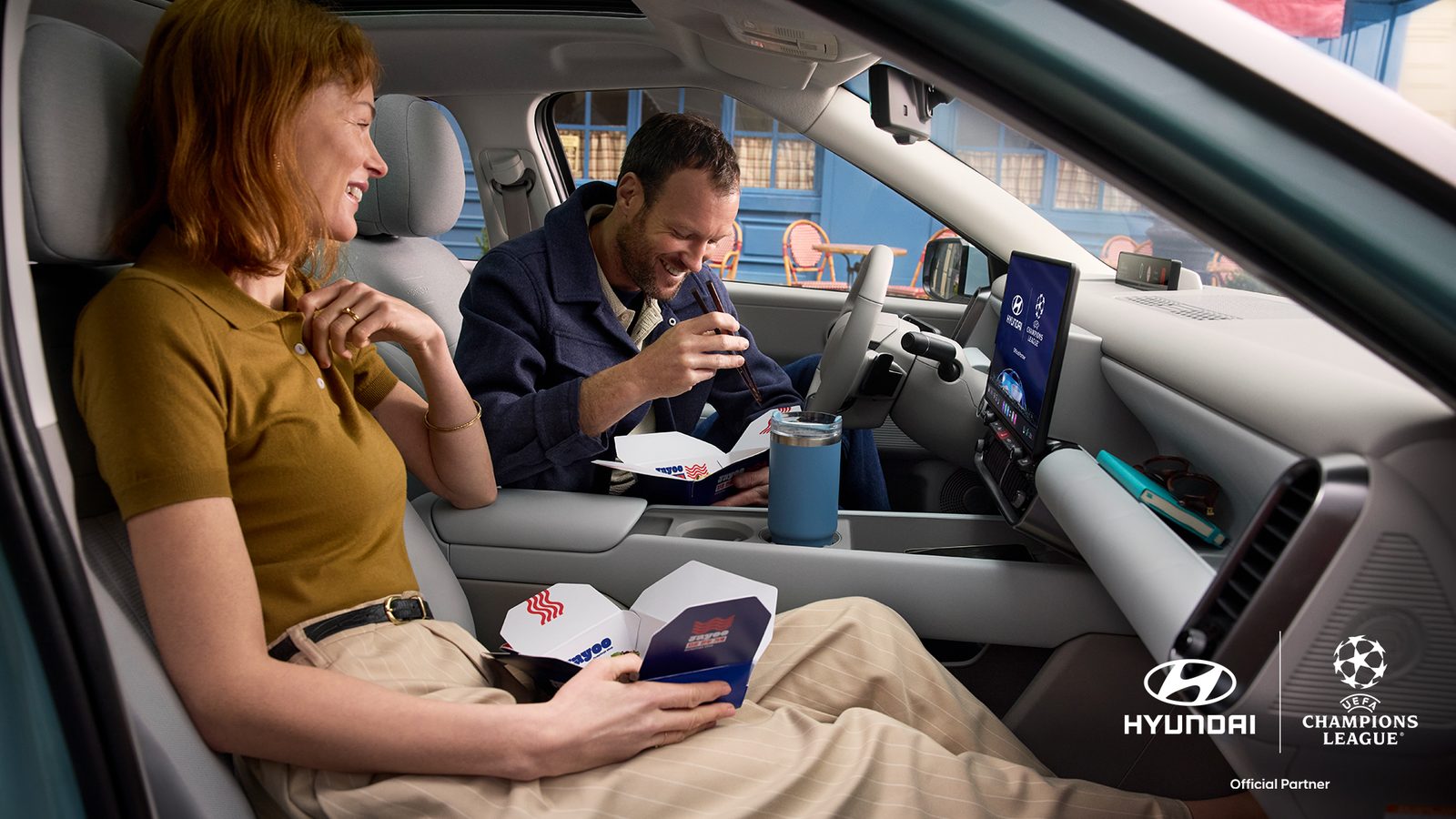 Egy férfi és egy nő a Hyundai IONIQ 3 első ülésein elvitelre rendelt ételt fogyaszt.
